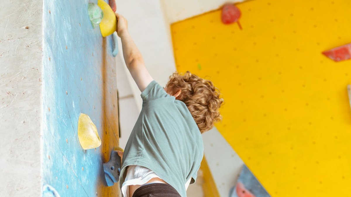 A young child bouldering on a colourful indoor climbing wall